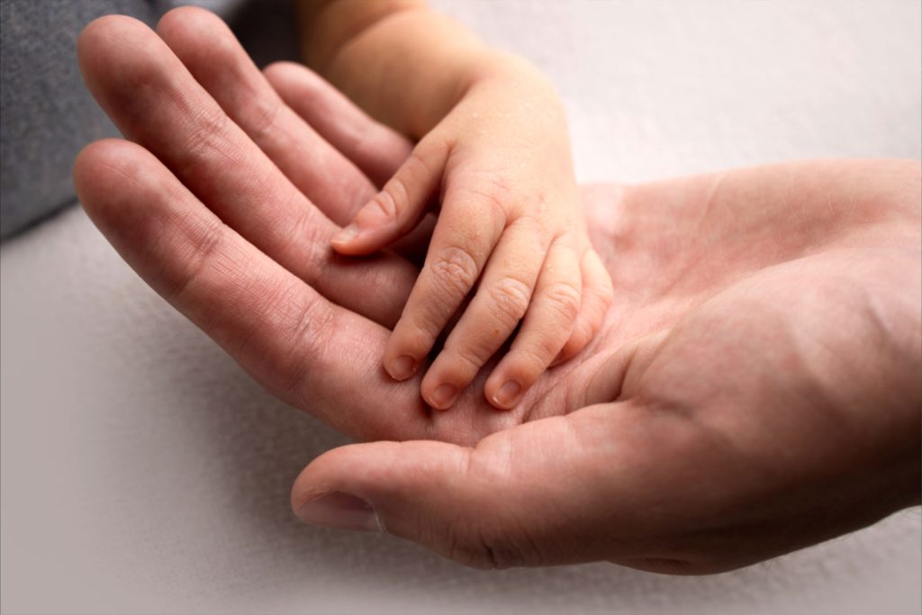 Adult hand cradling small child's hand symbolizing the parent-child bond and effects of separation