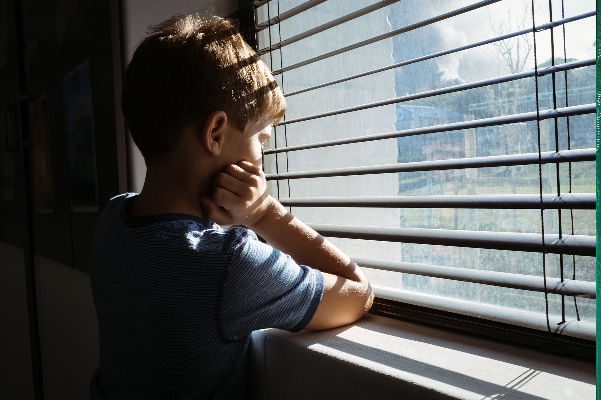 Young boy looking out window representing children of incarcerated parents