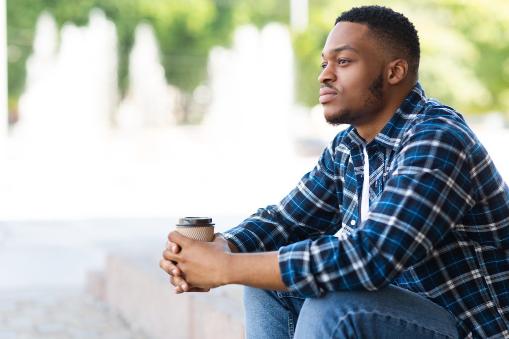 Young man sitting thoughtfully with coffee representing reflection on trauma bonding with parents