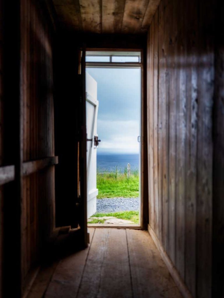 An open wooden door looking out to a bright coastal landscape — representing the first step toward healing and counselling support in Victoria, BC